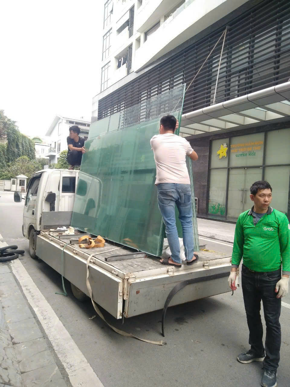 Nhân công phối hợp di chuyển các tấm kính lớn trên xe dưới ánh sáng ban ngày